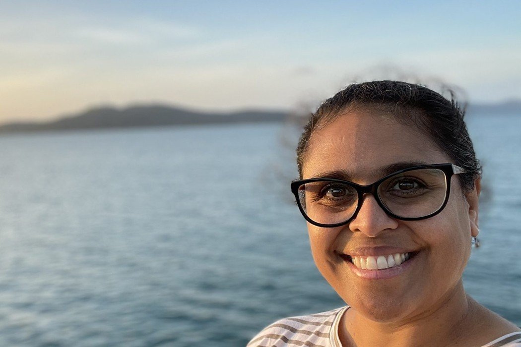 Rhianna Patrick, smiling, beside open water at sunset.