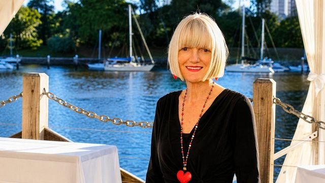 Linda Harnett photographed beside the water at a marina, sailing boats behind her.