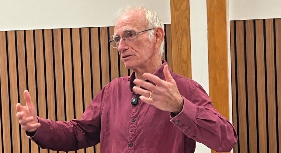 Dr Thom Blake speaking, both hands raised mid-sentence, at Mitchelton Library